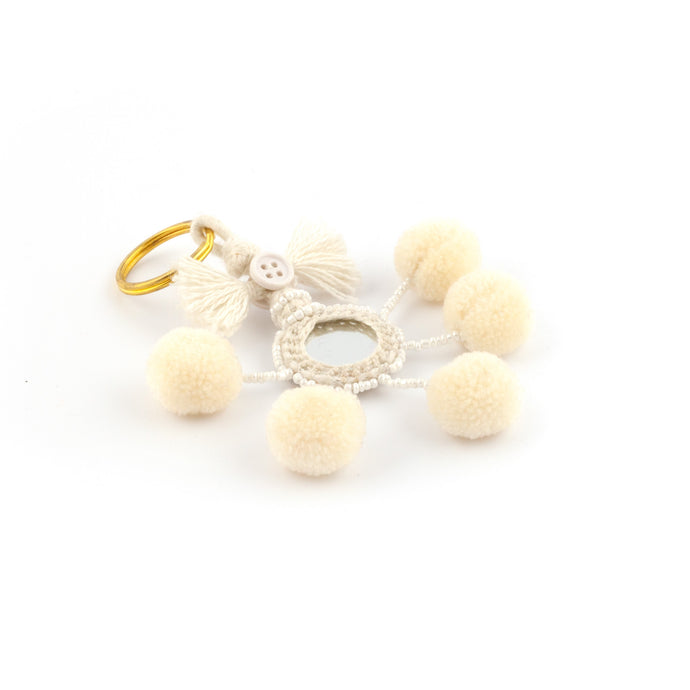 Nyckelring i vitt tillverkad av pompoms, garn, pärlor och spegel.  Med ring för fastsättning.  Längd exkl. ring: 10,5 cm.