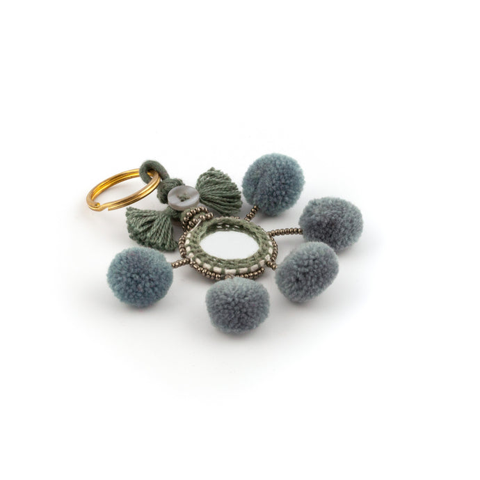 Nyckelring i grått tillverkad av pompoms, garn, pärlor och spegel.   Med ring för fastsättning.  Längd exkl. ring: 10,5 cm.