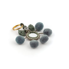 Ladda upp bild till galleriet Nyckelring i grått tillverkad av pompoms, garn, pärlor och spegel.   Med ring för fastsättning.  Längd exkl. ring: 10,5 cm.
