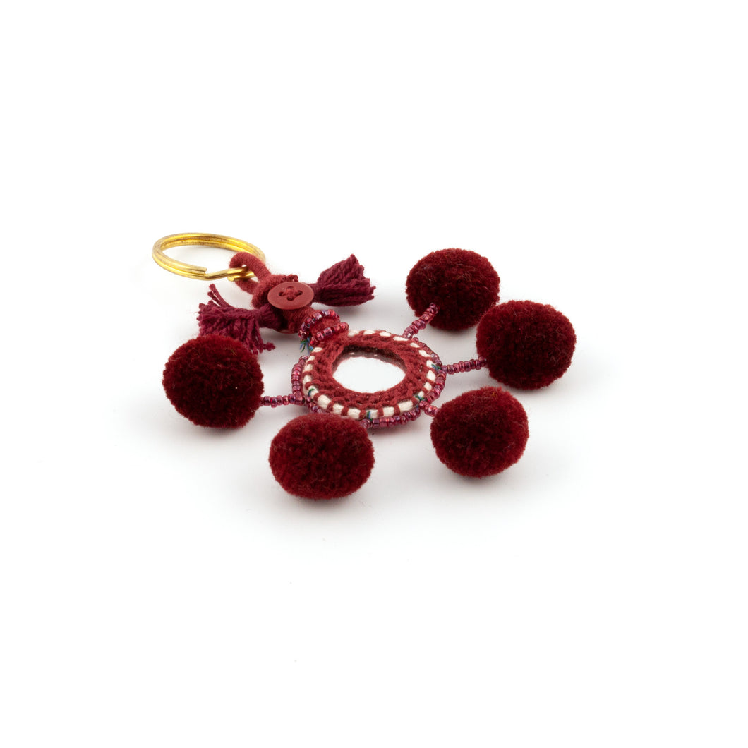 Nyckelring i vinrött tillverkad av pompoms, garn, pärlor och spegel.  Med ring för fastsättning.  Längd exkl. ring: 10,5 cm.