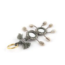 Ladda upp bild till galleriet Nyckelring i grått tillverkad av garn, pärlor, snäckor och speglar. Med ring för fastsättning.  Längd exkl. ring: 14 cm.
