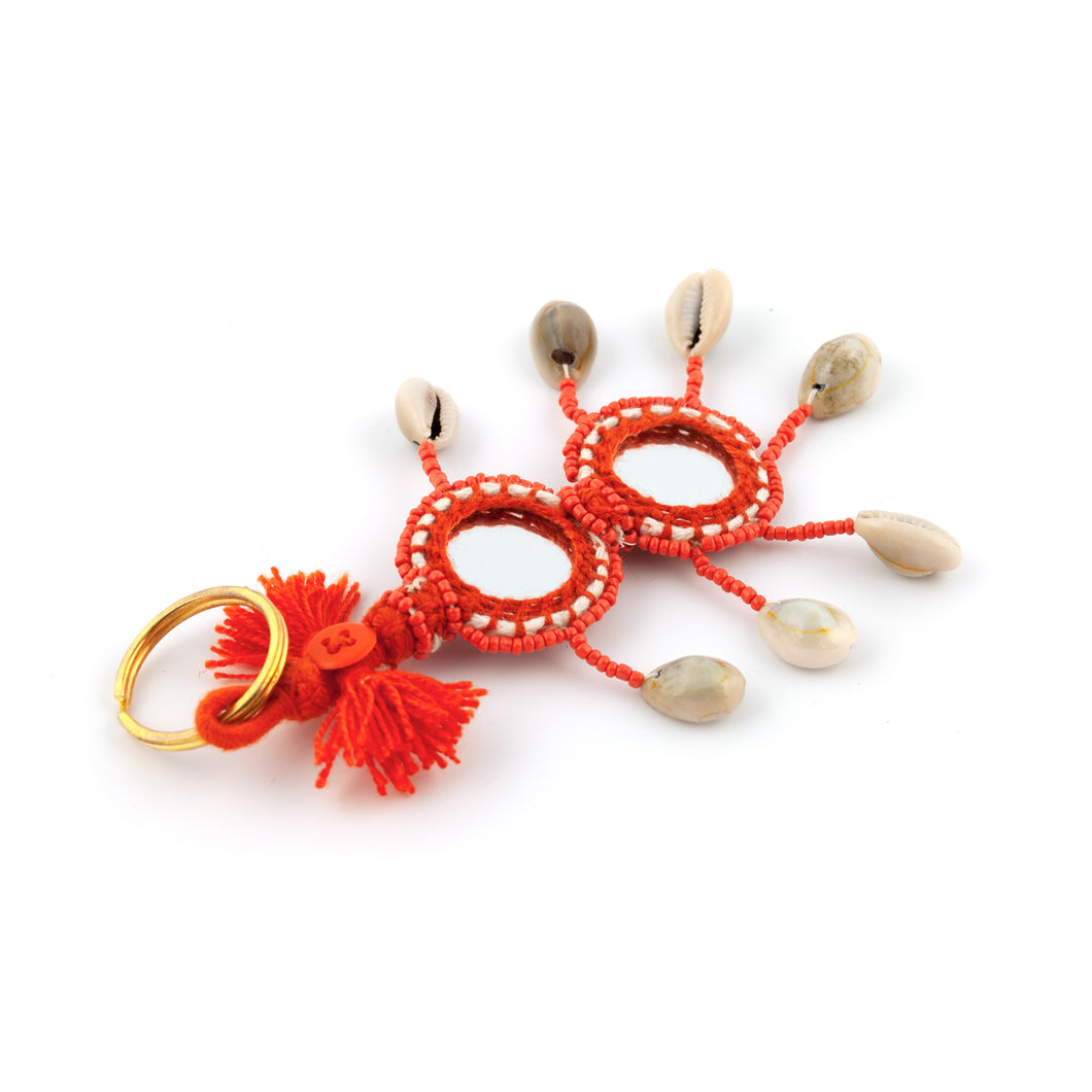 Nyckelring i orange tillverkad av garn, pärlor, snäckor och speglar. Med ring för fastsättning.  Längd exkl. ring: 14 cm.