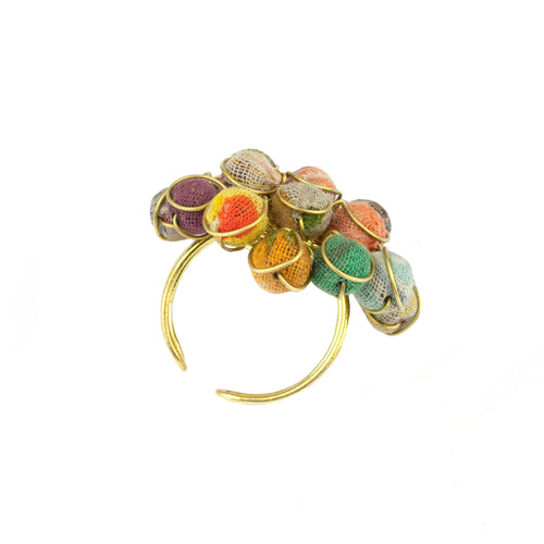 Ladda bild 1 i i galleriläge. Ring tillverkad av återvunnet material. Design i form av ett cirkelformat kluster av små olikfärgade tygkulor och detaljer av mässingsfärgad metall.Ringen är öppen baktill för att kunna justeras till att passa alla.  Storlek på bollarna: 3,7 cm i diameter