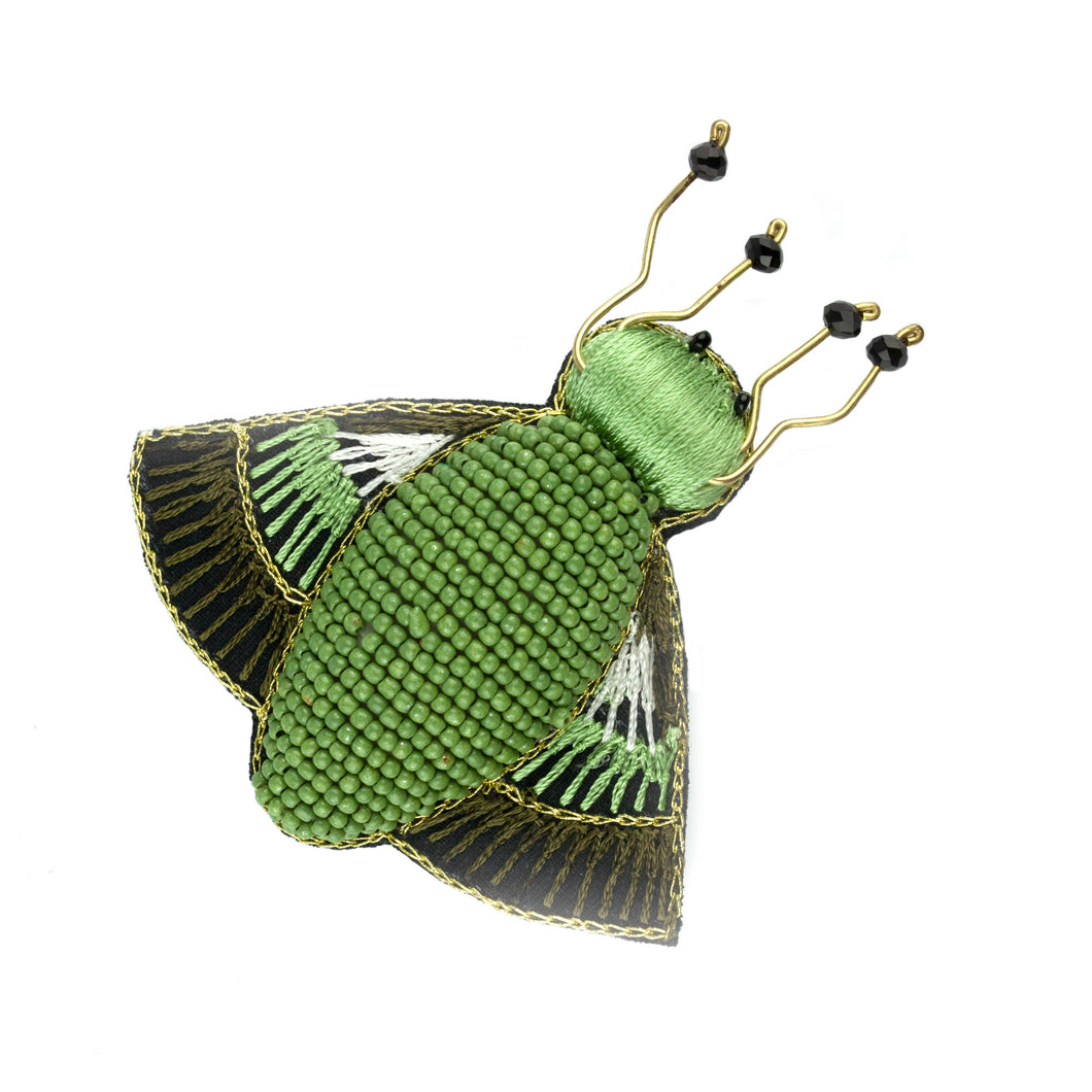 Brosch med en kropp av gröna pärlor, vingar och huvud av grönt, brunt och vitt garn samt detaljer av metall och svarta pärlor.  Storlek 8x7 cm.